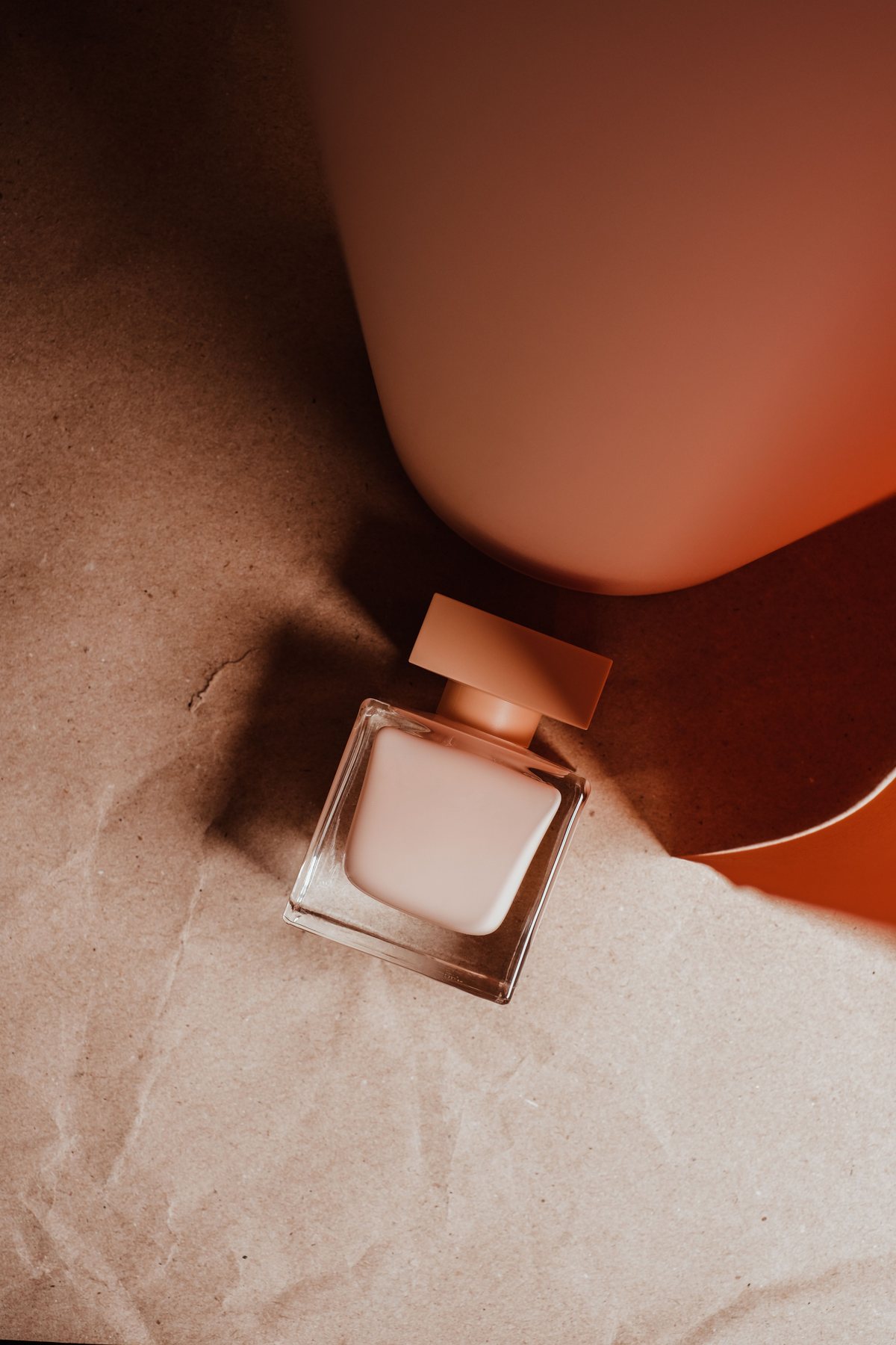 Minimal square perfume bottle photographed with warm geometric shadows.